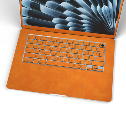 Orange scrub-textured synthetic leather MacBook skin. Wide keyboard and inside material detail. Air 15.3 M3-M5 shared material/installation illustration; actual cutouts and included pieces follow the selected model and coverage. Laptop not included.
